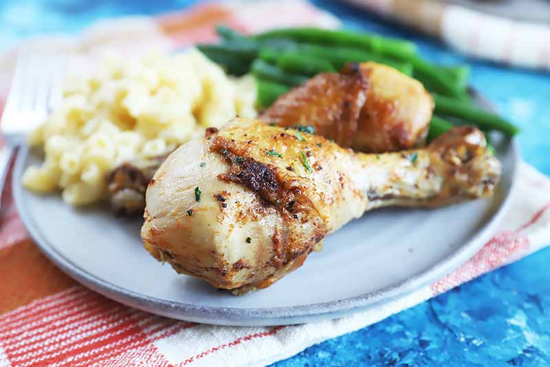 Horizontal image of drumsticks served with mashed potatoes and green beans on a plate on a red and white towel.