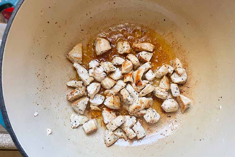 Horizontal image of cooking chunks of white meat in a pot with ground pepper.