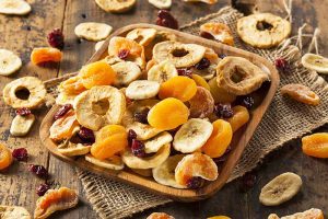Horizontal image of a wooden bowl filled with assorted dried fruit on a burlap napkin.