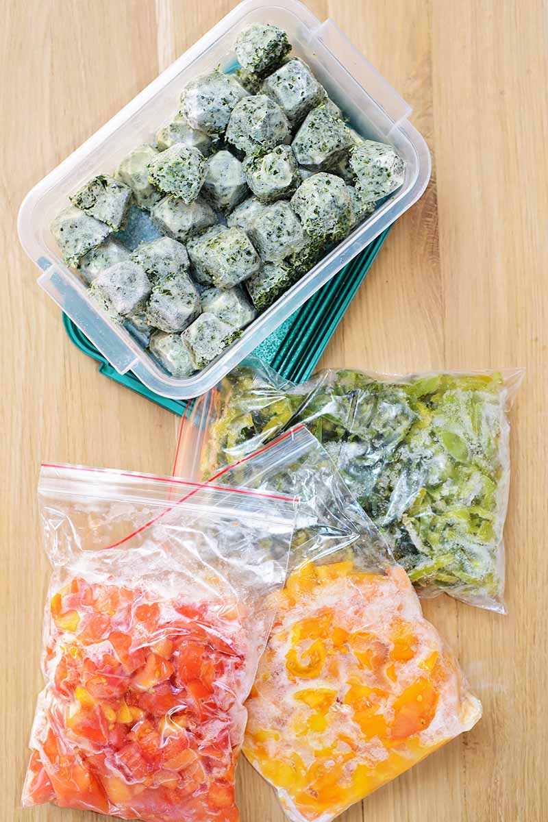 Vertical image of frozen vegetables in airtight bags and in a container on a wooden table.