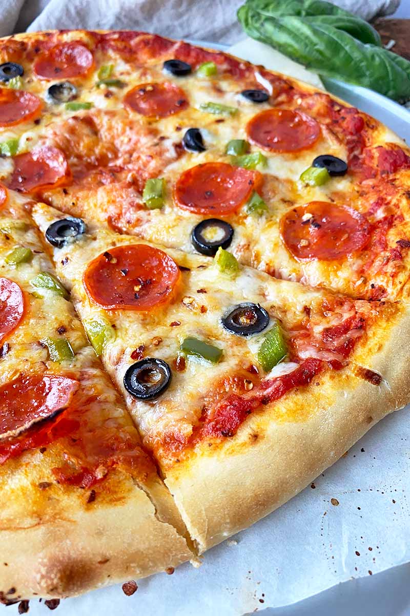 Vertical close-up image of a slice of flatbread topped with marinara sauce, pepperoni, olives, and green peppers.