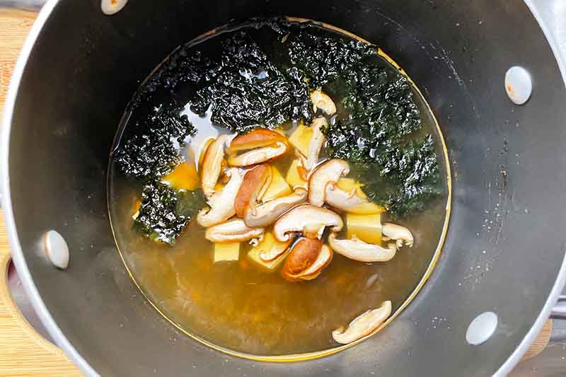 Horizontal image of broth, shiitake, and seaweed in a pot.