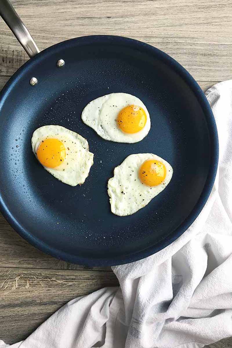 Vertical image of a nonstick skillet with fried eggs on a white towel.