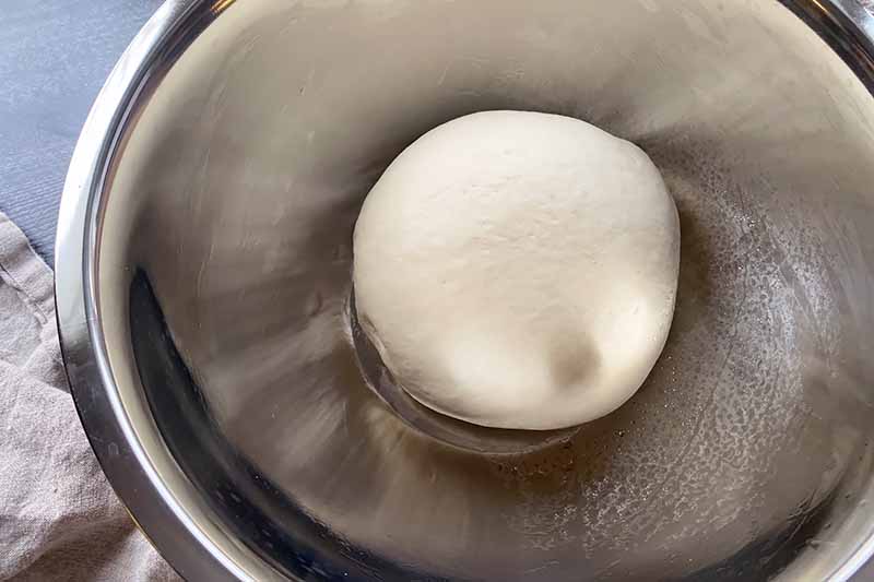 Horizontal image of a mound of dough in a metal bowl.