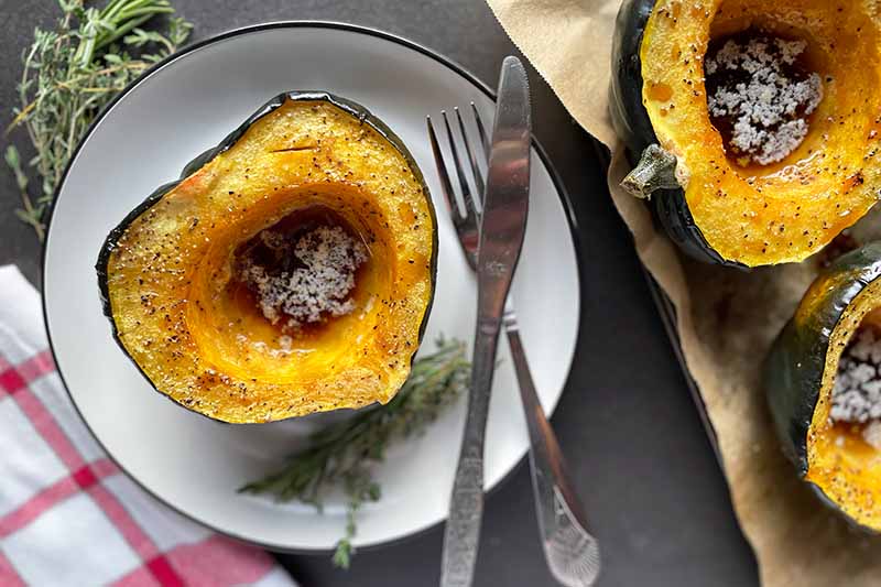 Horizontal image of roasted squash on a plate next to silverware and a towel.