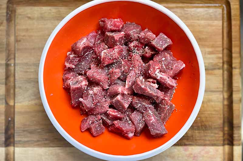 Horizontal image of a red plate with seasoned chunks of beef.