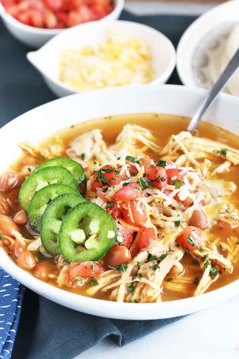 Vertical image of a Mexican chicken soup garnished with jalapeno peppers and salsa.
