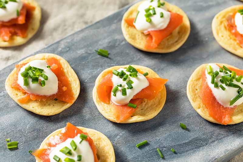 Horizontal image of small appetizers with smoked salmon and dollops of sour cream with chives on a slate.