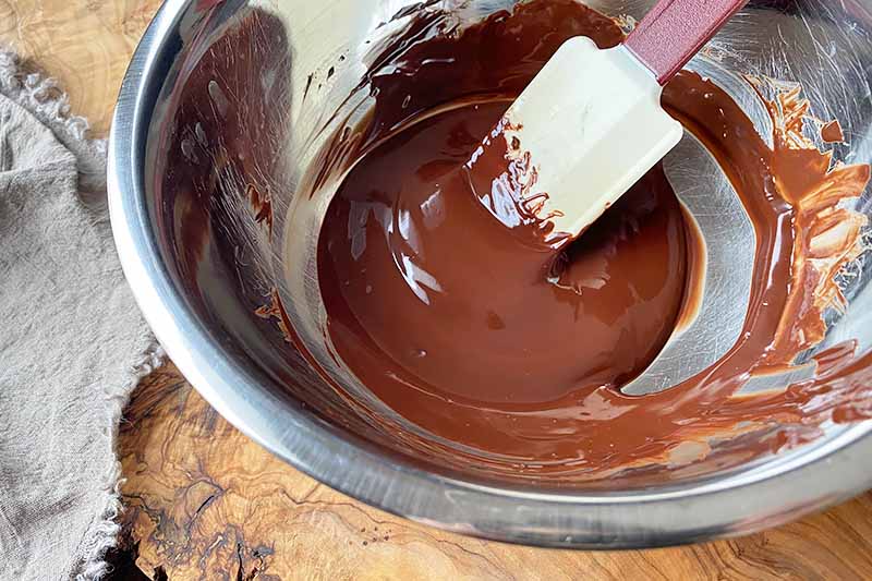 Horizontal image of melted chocolate stirred by a spatula in a metal bowl.