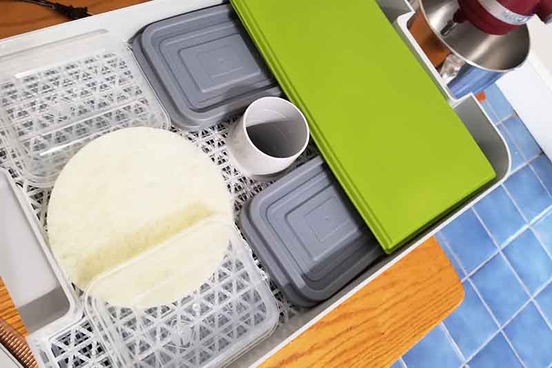 Horizontal image of the different parts to a kitchen appliance on a wooden table over a blue tiled floor.