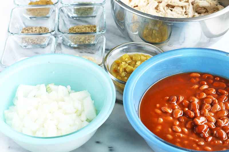 Horizontal image of bowls of measured meat, spices, beans, and chopped onions.