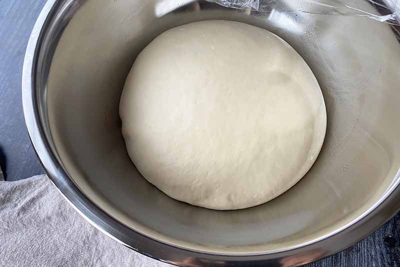 Horizontal image of a puffy mound of dough in a metal bowl.