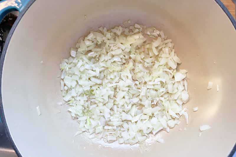 Horizontal image of sweating onions in a pot.