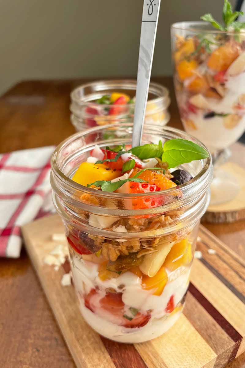 Vertical close-up image of the layers of a fruit parfait with a spoon inserted into it.