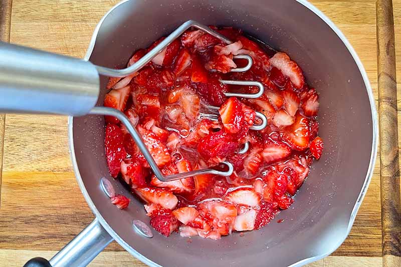 Horizontal image of mashing red fruit in a pot.