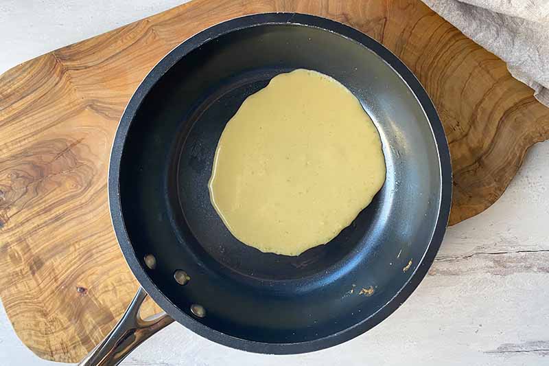 Horizontal image of a small round of yellow batter in a nonstick skillet.