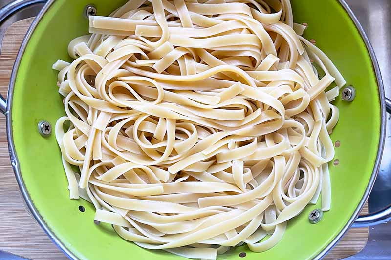 Horizontal image of draining cooked fettuccine in a green colander.