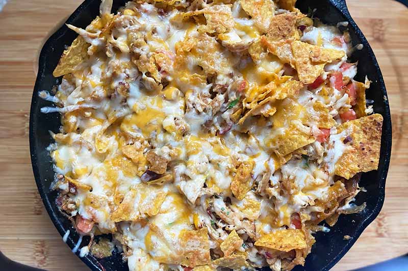 Horizontal image of a cast iron skillet with nachos topped with melted cheese.