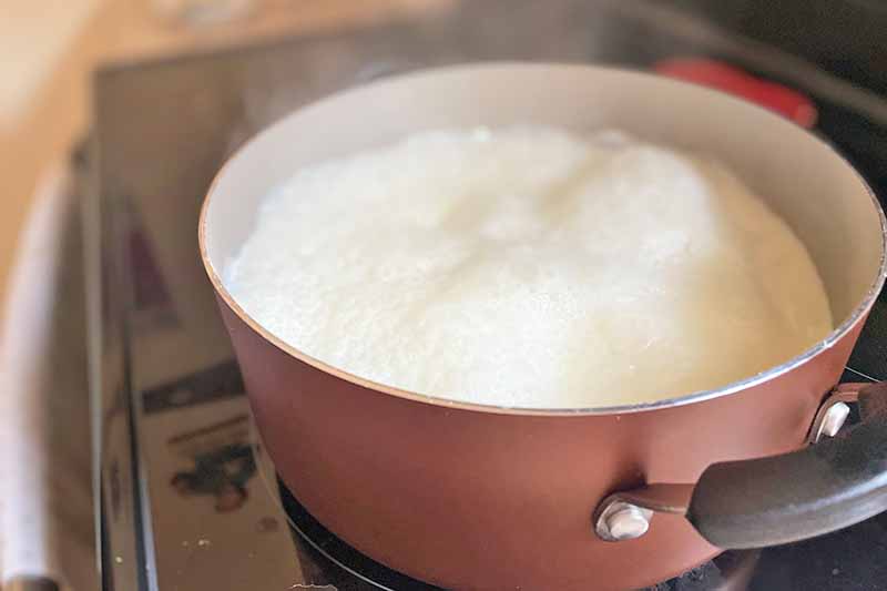 Horizontal image of boiling cream in a pot on the stove.