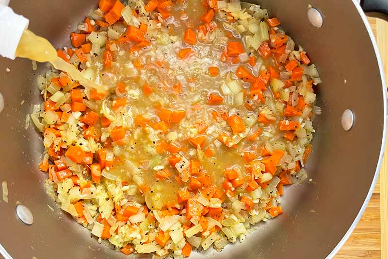 Horizontal image of cooking chopped vegetables in broth in a pot.