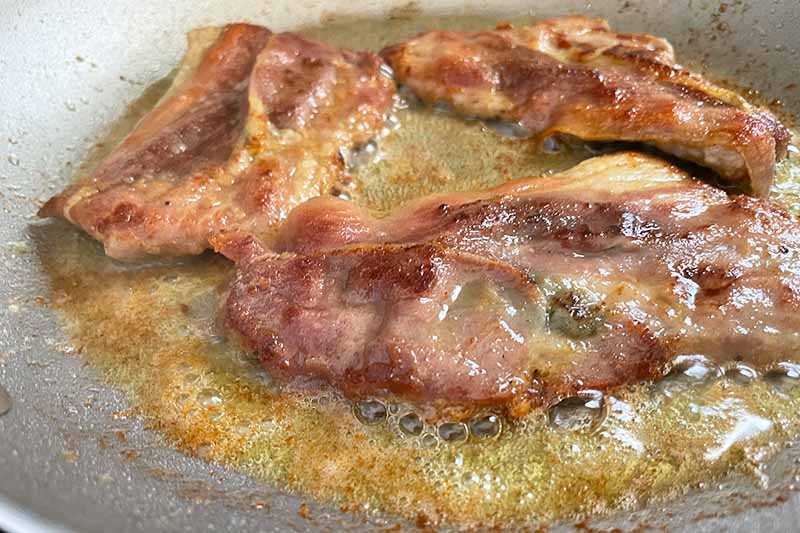 Horizontal image of lightly frying slices of meat in a shallow pan with oil.