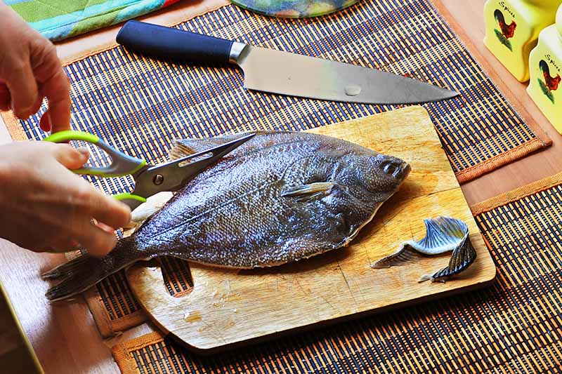 Horizontal image of cutting a whole fish on a wooden cutting board.