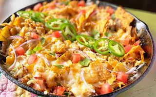Horizontal image of a one-pan recipe with nachos, salsa, jalapeno, and melted cheese.