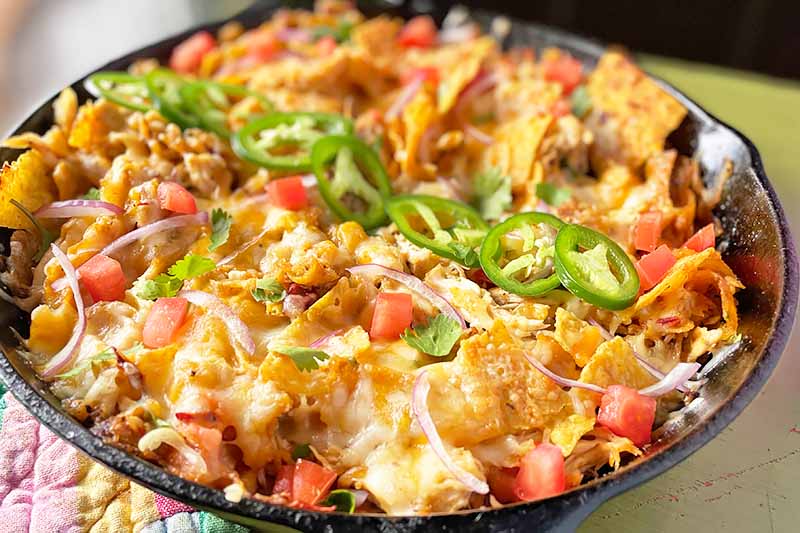 Horizontal image of a one-pan recipe with nachos, salsa, jalapeno, and melted cheese.