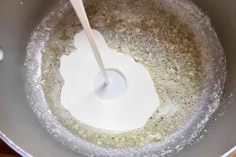 Horizontal image of pouring cream into a garlic and oil mixture in a pot.