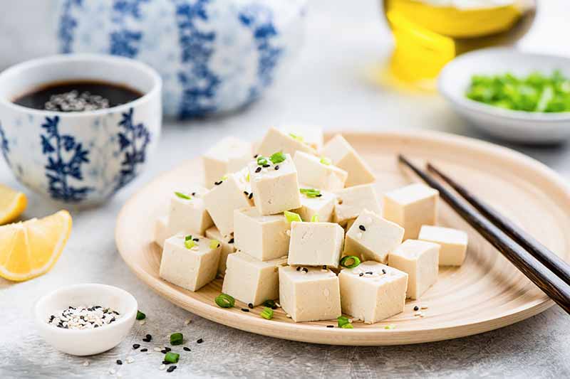 Horizontal image of a tan plate with a pile of tofu cubes next to soy sauce and chopsticks.