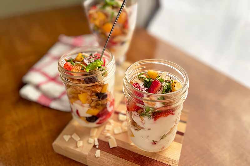 Horizontal image of glass jars filled with layers of yogurt and berries on a wooden table.
