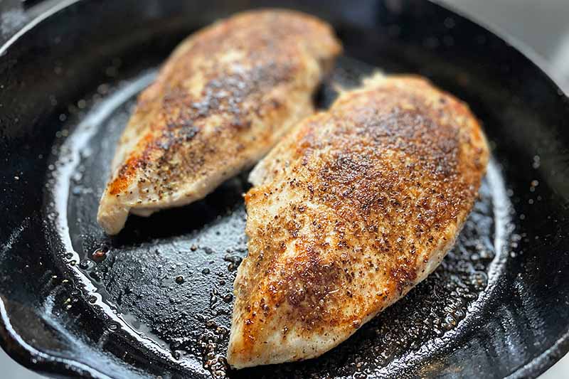Horizontal image of searing seasoned chicken breasts in a pan.