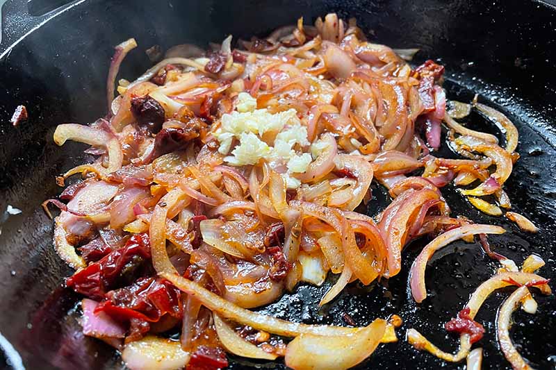 Horizontal image of cooked peppers, onions, and garlic in a cast iron pan.