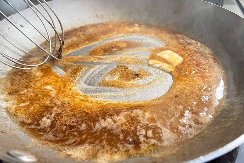 Horizontal image of whisking butter into a brown sauce in a pan.
