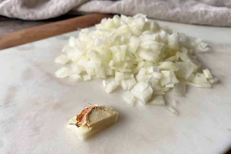Horizontal image of a pile of diced onions next to a root end.