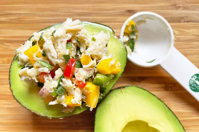 Horizontal image of stuffing a seafood salad in an avocado half with a tablespoon.
