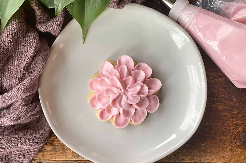 Horizontal image of three layers of thick pink frosting on a floral shaped cookie on a white plate.
