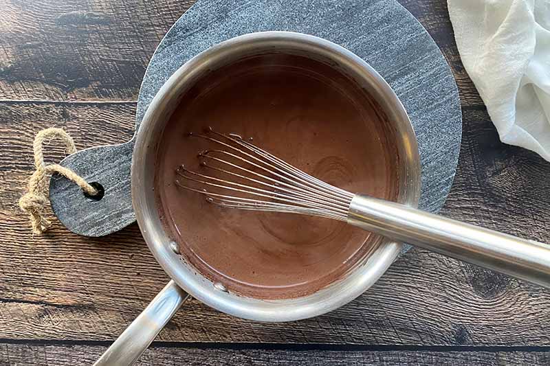 Horizontal image of whisking a dark brown liquid in a pot.