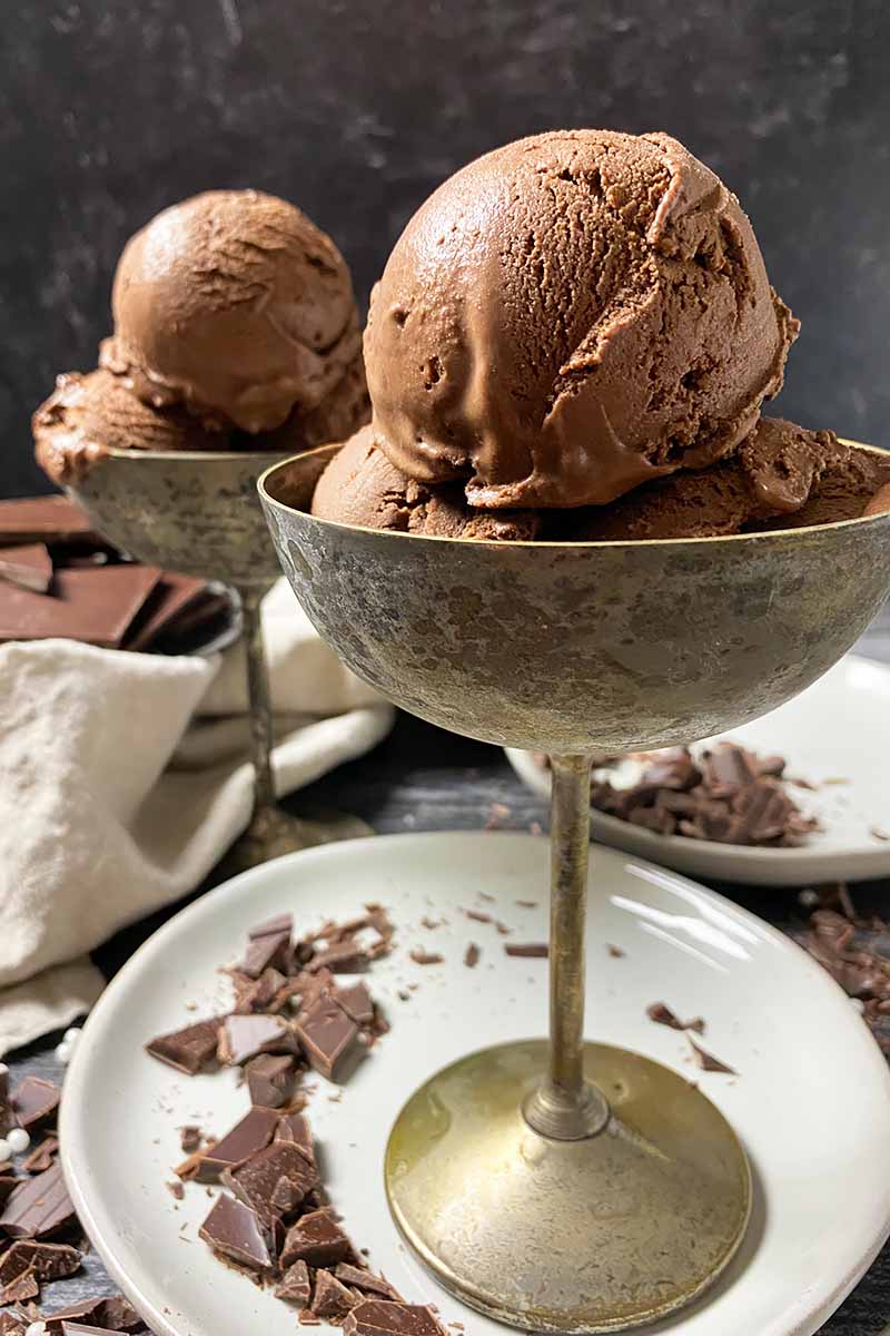 Vertical image of metal goblets with scoops of a dark brown frozen dessert on white plates.