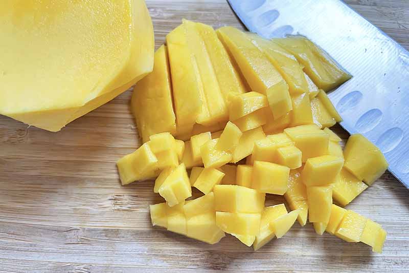 Horizontal image of a cubed fresh mango next to a knife.