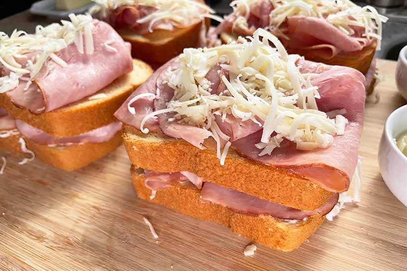 Horizontal image of layers of shredded cheese, ham slices, and bread.