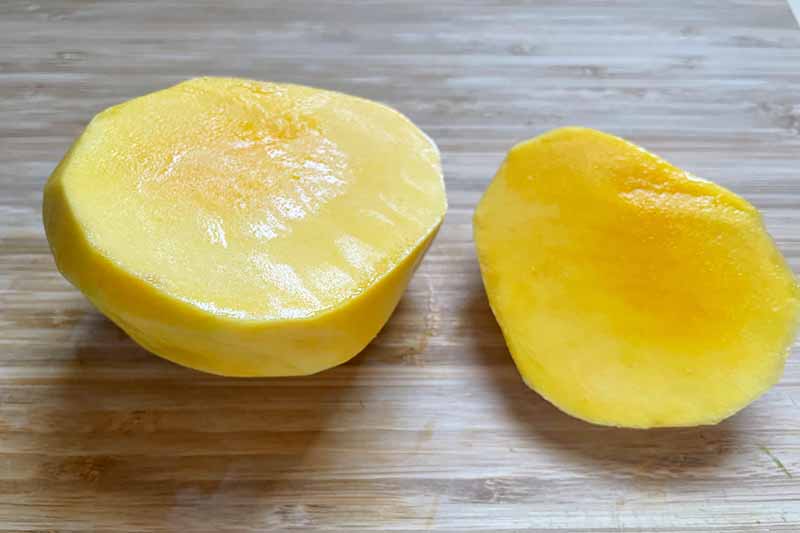 Horizontal image of a peeled and sliced mango on a wooden cutting board.