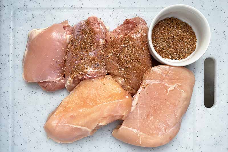 Horizontal image of spreading seasoning on raw pieces of poultry.