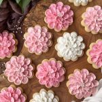 Horizontal top-down image of assorted pink and white decorated baked goods on a wooden surface.