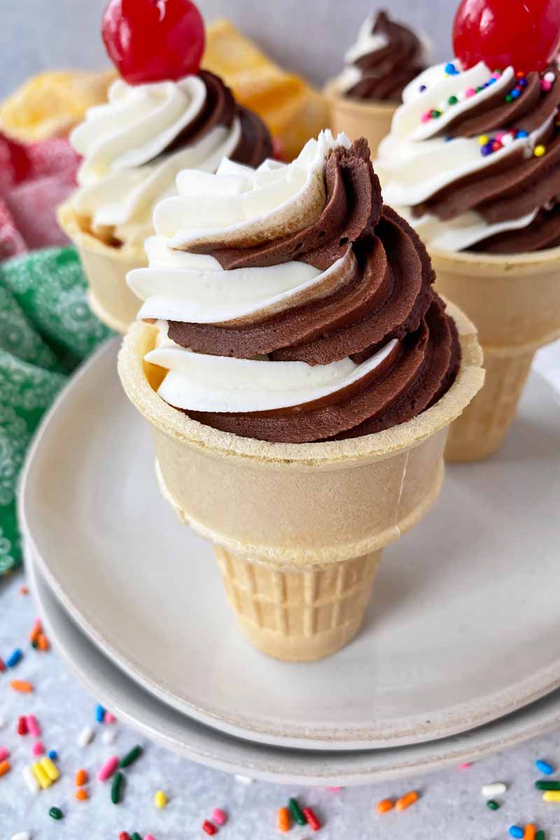 Vertical image of swirls of chocolate and vanilla frosting on top of a sugar cone.
