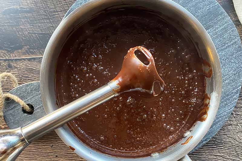 Horizontal image of an immersion blender over a pot with a thick dark brown liquid.