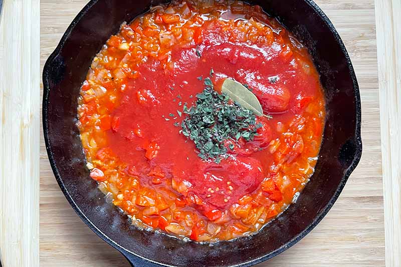Horizontal image of cooking tomato sauce and aromatics in a cast iron skillet.