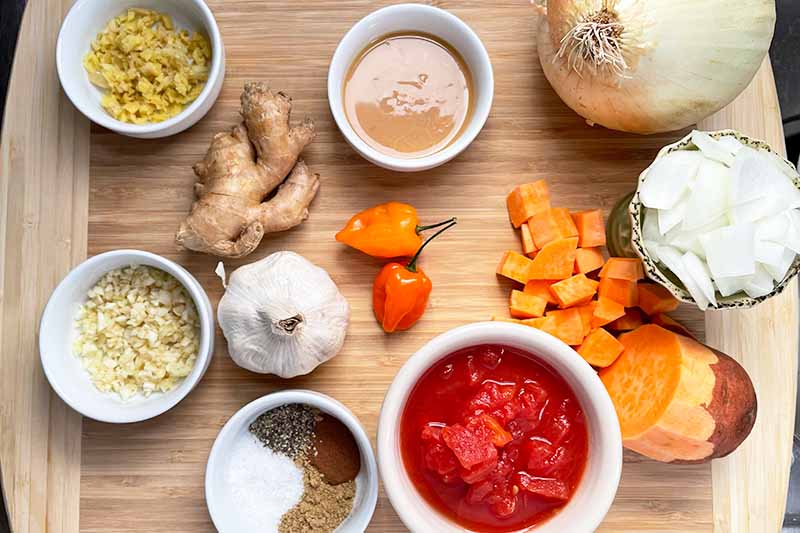Horizontal image of assorted ingredients measured out in white bowls with some scattered on a wooden cutting board.