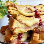 Horizontal image of a stacked sandwich with melted cheese and ham, with a drizzle of jam.