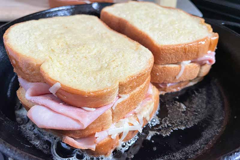 Horizontal image of searing two sandwiches in a cast iron skillet.